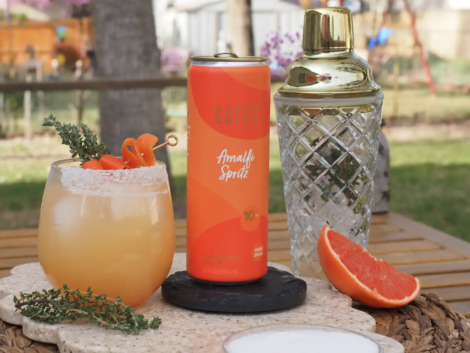 Cocktail with a can of Amalfi Spritz and a cocktail shaker on a table outdoors.