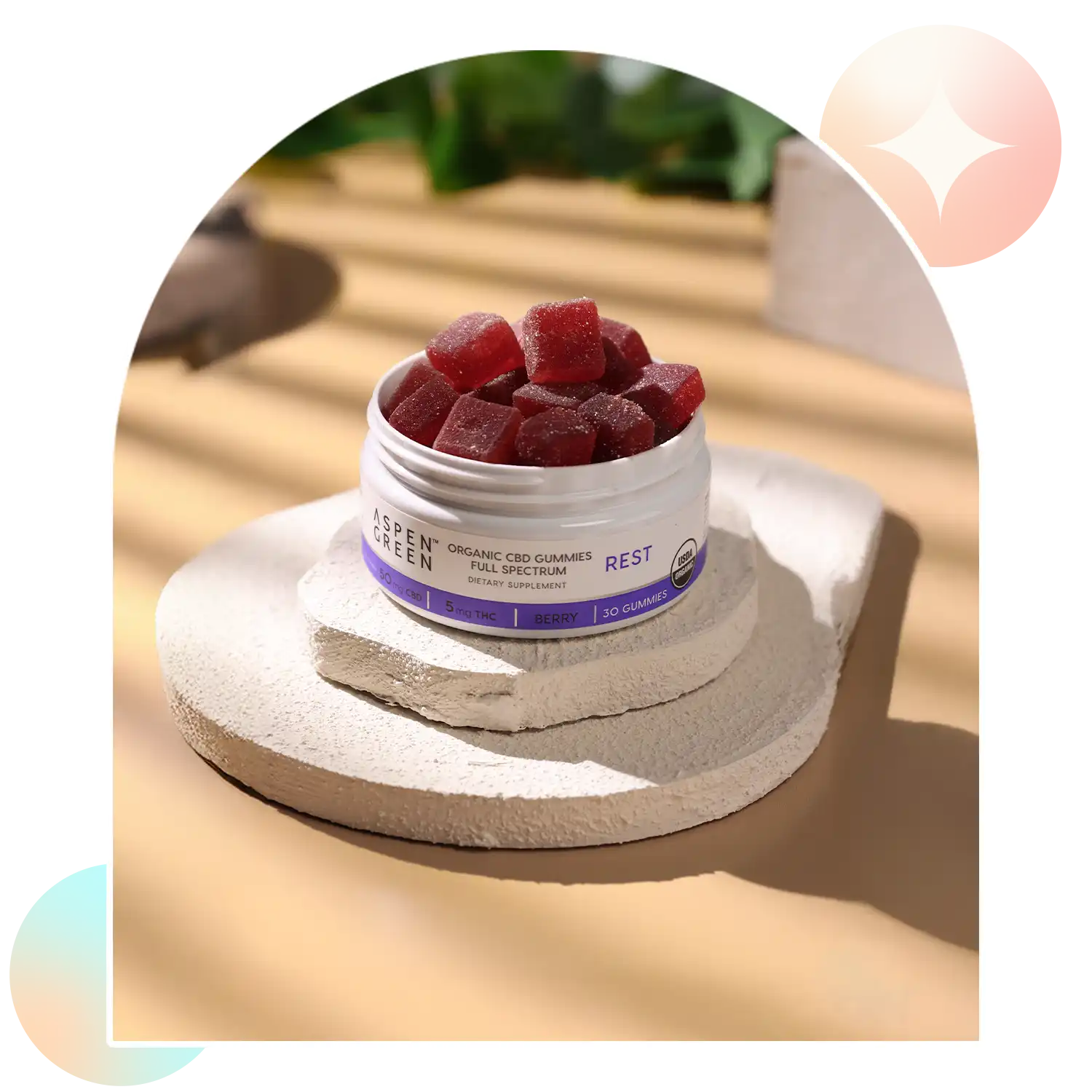 Open jar of Aspen Green USDA Certified Organic Rest CBD Gummies on a stone surface with a blurred outdoor background.