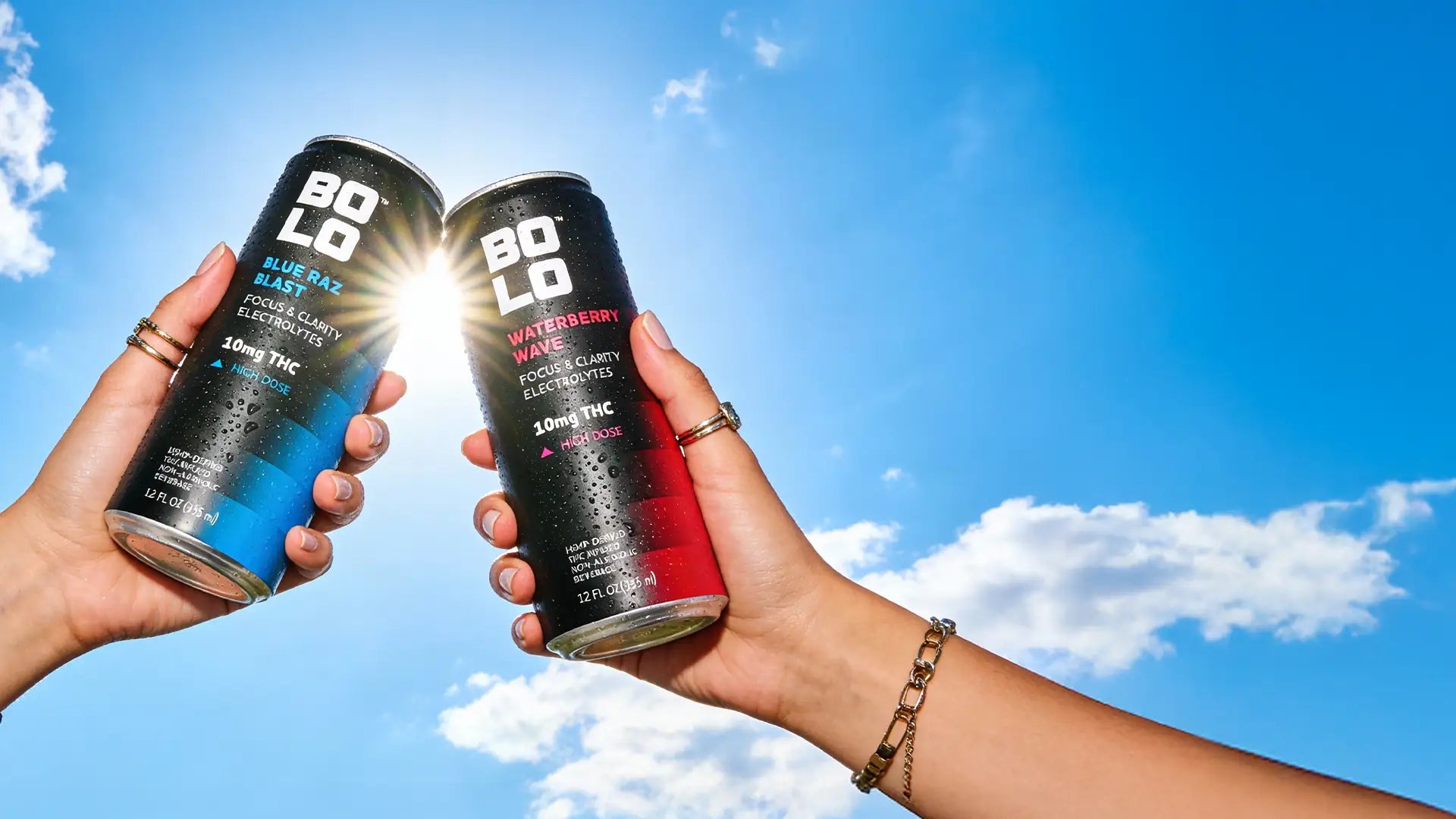 Two hands holding Bolo THC drink cans against a blue sky.