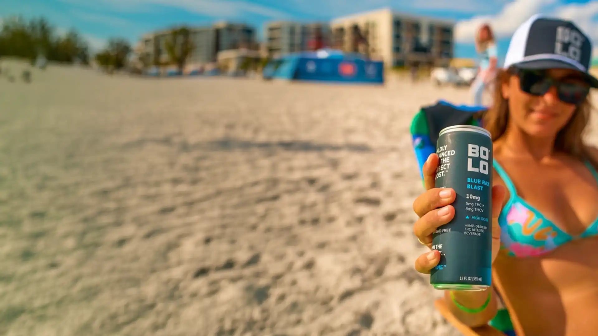 Woman on a beach holding a can of BOLO Blue Raz Blast