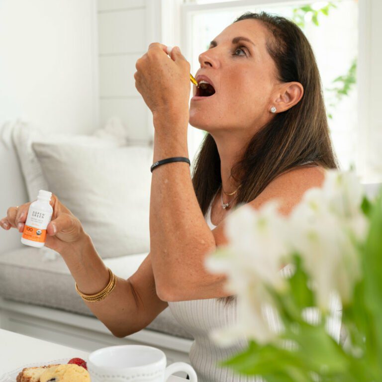 Woman enjoying breakfast at a table while taking a dropper of Extra Citrus CBD oil.