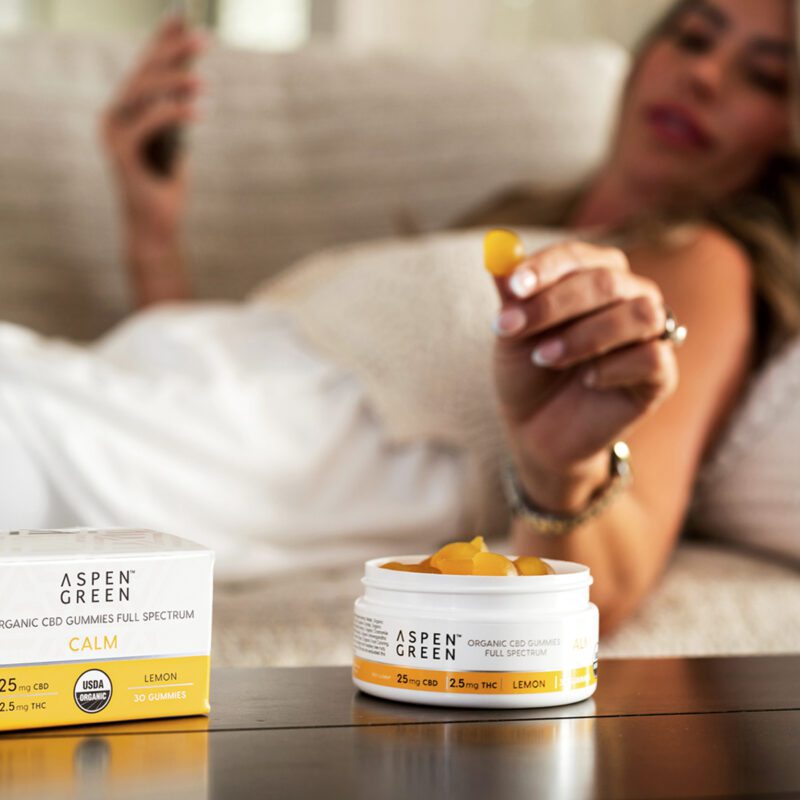 Woman grabbing Aspen Green CBD calm gummy on couch