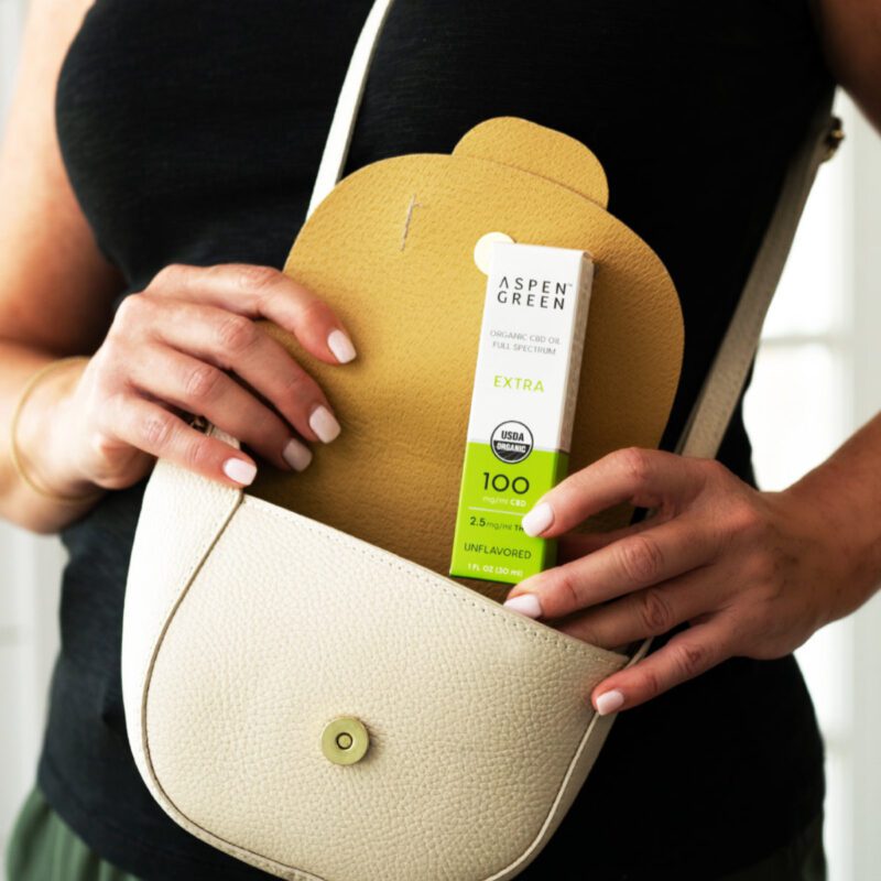 Woman putting Aspen Green Extra Unflavored CBD Oil box in purse