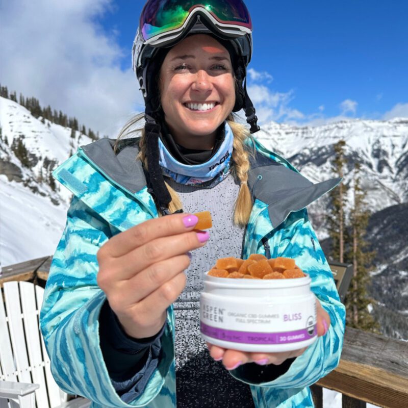 Happy skier indulging in Aspen Green Bliss Gummies while skiing down a snowy slope
